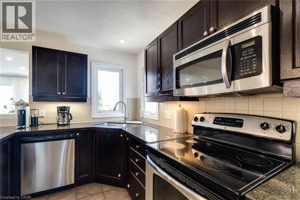 Kitchen featuring dark wood cabinetry, stainless steel appliances, granite countertops, and a tiled backsplash - 928 Dunblane Court, Kitchener, ON