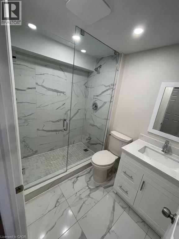 Modern bathroom featuring a frameless glass shower enclosure, white marble-look tile flooring, and a coordinating vanity with an integrated sink - 928 Dunblane Court, Kitchener, ON