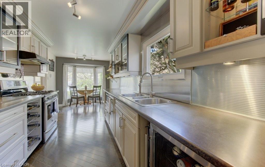 Galley kitchen featuring wood-finish flooring, light cabinetry, stainless steel appliances, and a double basin sink - 108 Clearwater Crescent, Waterloo, ON