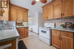 Kitchen featuring electric stove, tasteful backsplash, ceiling fan, light countertops, and wood finish cabinetry - 