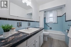 Bathroom with tile walls, a wainscoted wall, vanity, shower / tub combo, and dark wood-type flooring - 