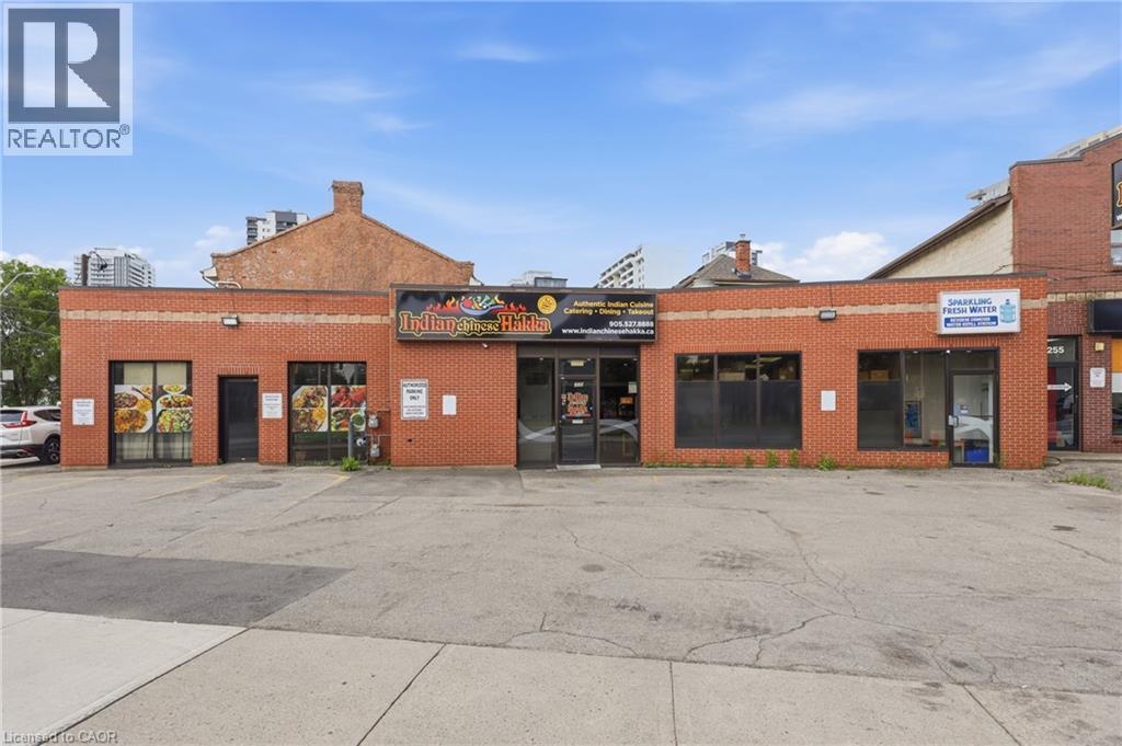 Brick commercial building with multiple storefronts and a paved parking area - 239 York Boulevard, Hamilton, ON
