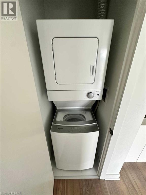 Stackable washer and dryer unit within a dedicated alcove, featuring white appliances and wood-finish flooring - 2782 Barton Street E, Hamilton, ON