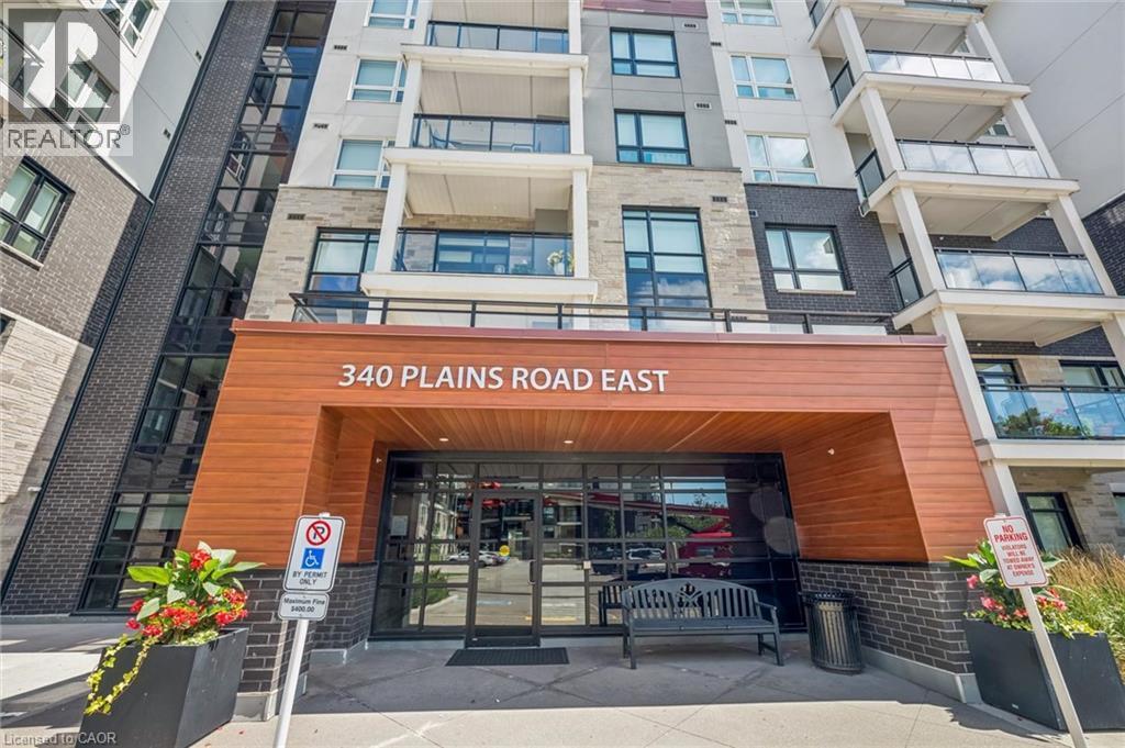 Modern building exterior featuring a wood-finish entrance canopy, dark brick accents, and stone facade - 340 Plains Road E Unit# 507, Burlington, ON - Outdoor With Balcony