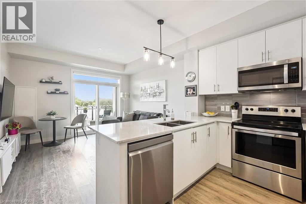 Open-concept living space featuring a modern kitchen with white cabinetry, stainless steel appliances, and light-toned countertops - 340 Plains Road E Unit# 507, Burlington, ON - Indoor Photo Showing Kitchen With Stainless Steel Kitchen With Double Sink