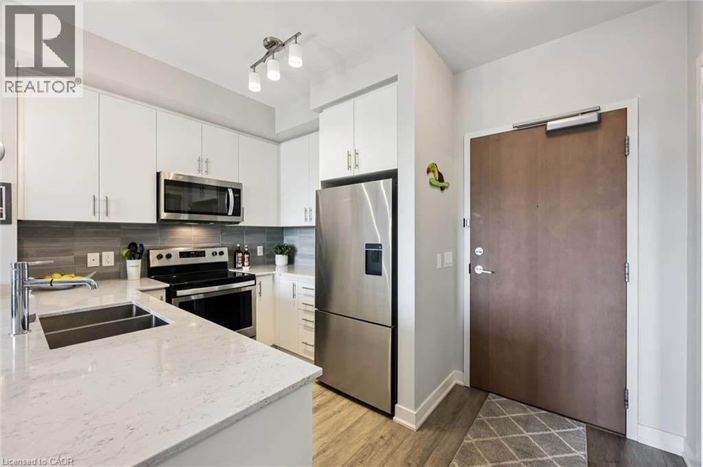 Modern kitchen featuring white cabinetry, light-toned countertops, and a gray tile backsplash - 340 Plains Road E Unit# 507, Burlington, ON - Indoor Photo Showing Kitchen With Stainless Steel Kitchen With Double Sink With Upgraded Kitchen