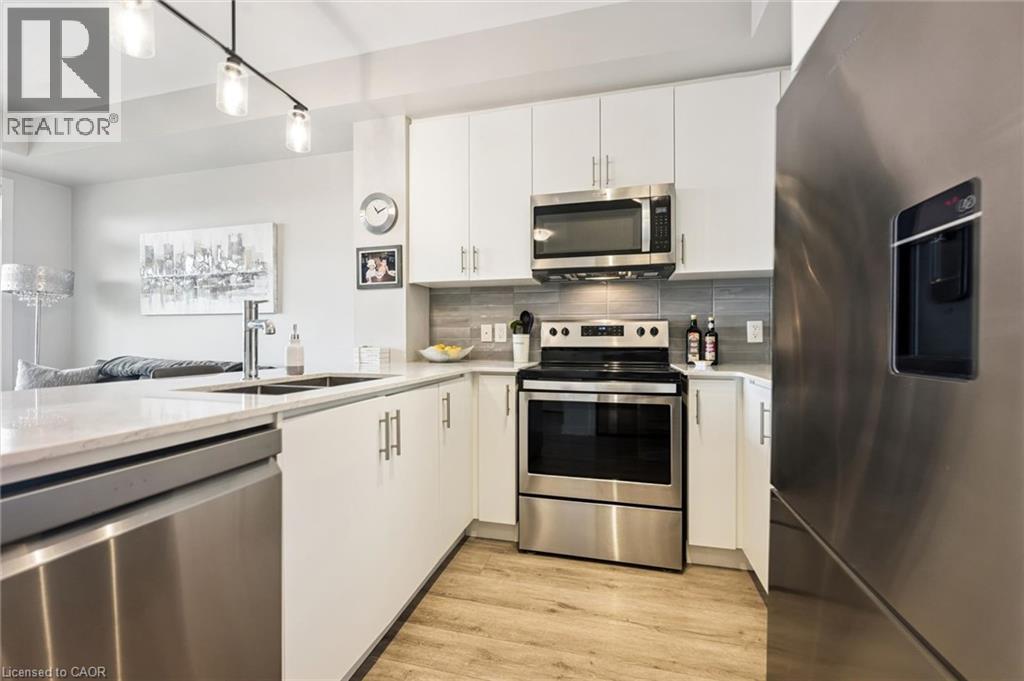 Well-appointed kitchen featuring white cabinetry, stainless steel appliances, a grey tiled backsplash, wood-finish flooring, and track lighting - 340 Plains Road E Unit# 507, Burlington, ON - Indoor Photo Showing Kitchen With Stainless Steel Kitchen With Double Sink