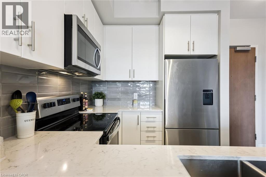 Modern kitchen featuring white cabinetry, a stainless steel appliance suite, light-colored countertops, and a gray subway tile backsplash - 340 Plains Road E Unit# 507, Burlington, ON - Indoor Photo Showing Kitchen With Stainless Steel Kitchen With Double Sink With Upgraded Kitchen