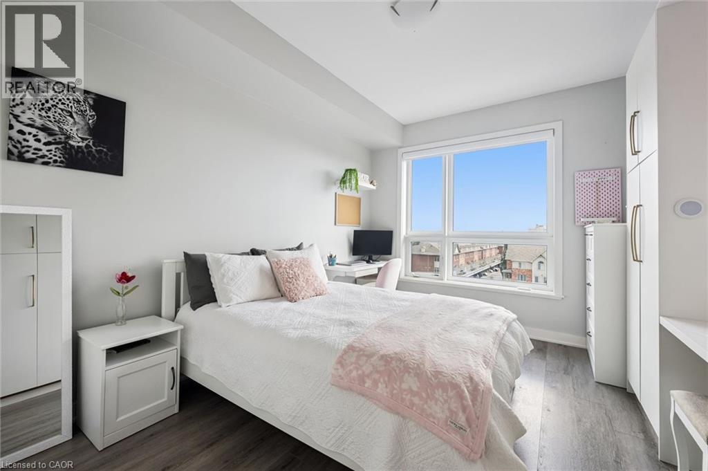 Bright room featuring a large window, wood-finish flooring, white walls, and built-in white cabinetry - 340 Plains Road E Unit# 507, Burlington, ON - Indoor Photo Showing Bedroom