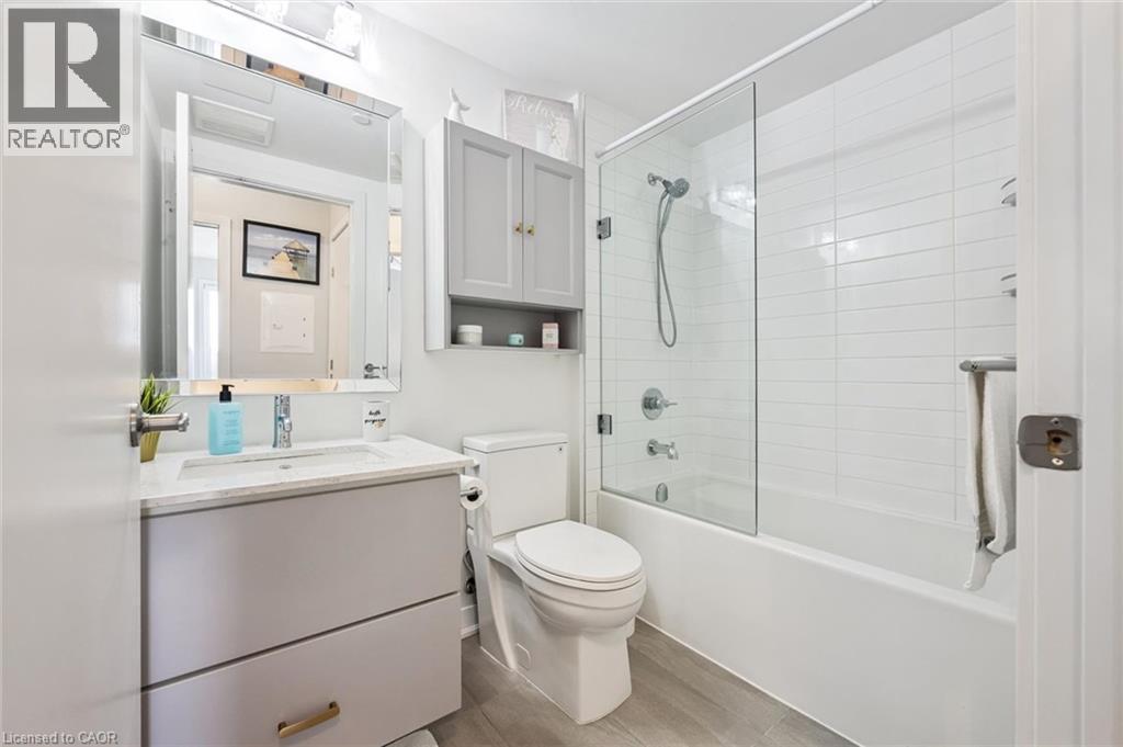 Contemporary bathroom featuring a grey vanity with a white countertop and undermount sink, a framed mirror, a wall-mounted medicine cabinet, a toilet, and a combined bathtub and shower with a glass en - 340 Plains Road E Unit# 507, Burlington, ON - Indoor Photo Showing Bathroom