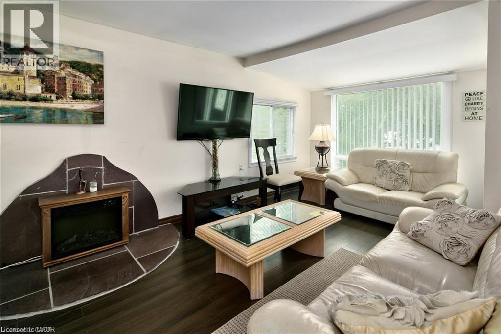 Living area featuring a floor-to-ceiling window with vertical blinds, wood-finish flooring, and a stone-clad fireplace with an electric insert - 42 5Th Lane, Wasaga Beach, ON - Indoor Photo Showing Living Room