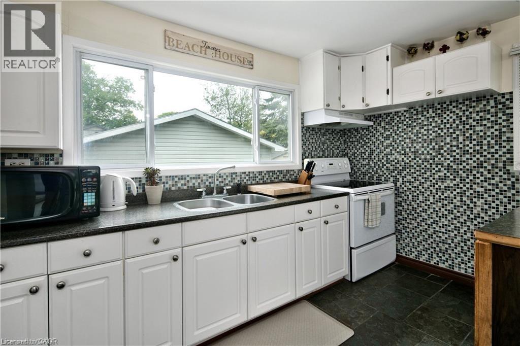 Kitchen featuring white cabinetry with dark hardware, dark countertop, a mosaic tile backsplash, and dark tile flooring - 42 5Th Lane, Wasaga Beach, ON - Indoor Photo Showing Kitchen With Double Sink