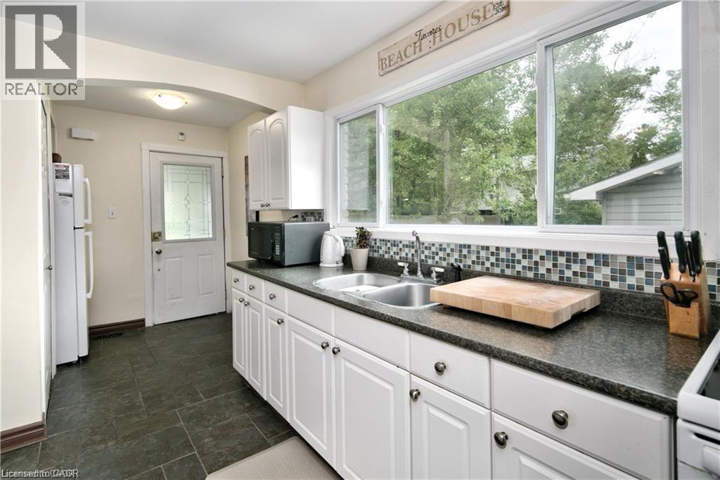 Kitchen featuring white cabinetry with dark hardware, dark countertops, and a mosaic tile backsplash - 42 5Th Lane, Wasaga Beach, ON - Indoor Photo Showing Kitchen With Double Sink