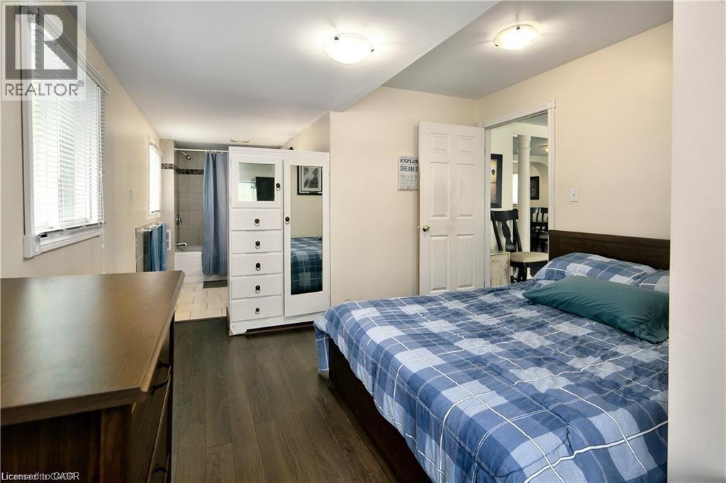 Bedroom featuring wood-finish flooring, an adjacent three-piece bathroom with a tiled shower, and a pair of windows with blinds - 42 5Th Lane, Wasaga Beach, ON - Indoor Photo Showing Bedroom