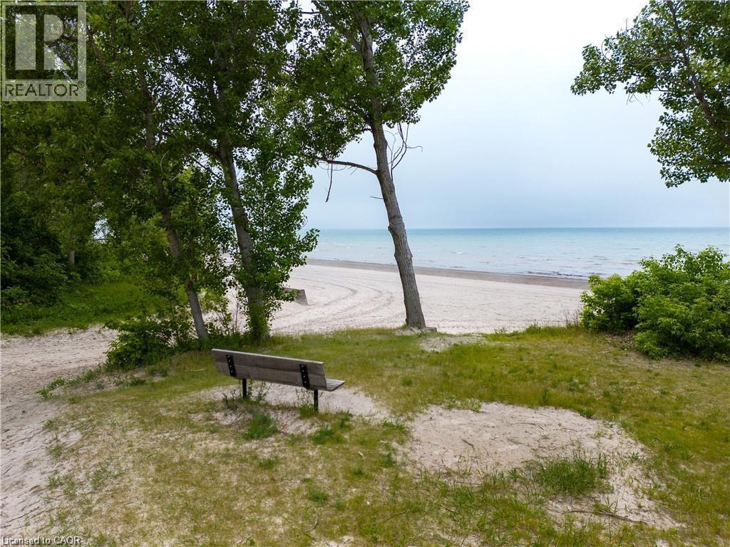 Sandy beachfront area featuring mature trees and a wooden bench - 42 5Th Lane, Wasaga Beach, ON - Outdoor With Body Of Water With View