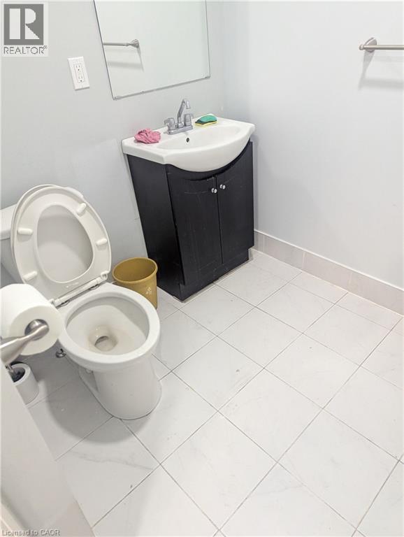 Bathroom featuring a white toilet, black vanity with a white basin sink, and a wall-mounted mirror - 499 Main Street E, Hamilton, ON
