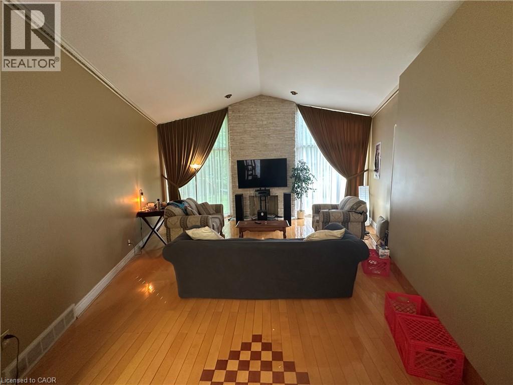 Spacious living area featuring a vaulted ceiling with crown molding, a stone-clad fireplace, and wood-finish flooring with a decorative inlay - 11 Wilmont Court, Hamilton, ON