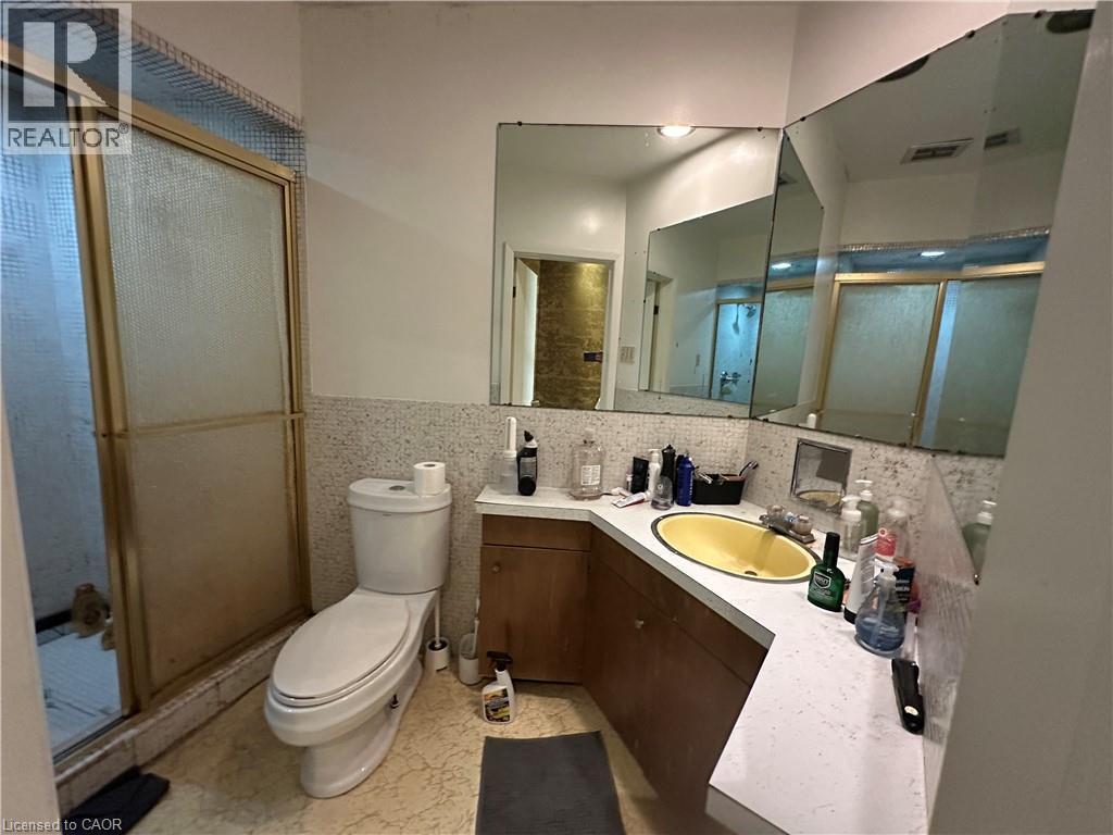 Bathroom featuring a corner vanity with a yellow oval sink, a built-in mirror, and a shower enclosure with a gold-tone frame - 11 Wilmont Court, Hamilton, ON