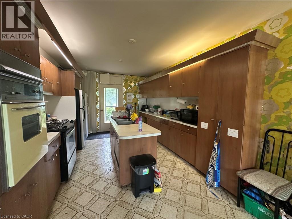 Kitchen featuring wood-finish cabinetry, a central island with an integrated sink, a built-in double oven, and a gas range - 11 Wilmont Court, Hamilton, ON