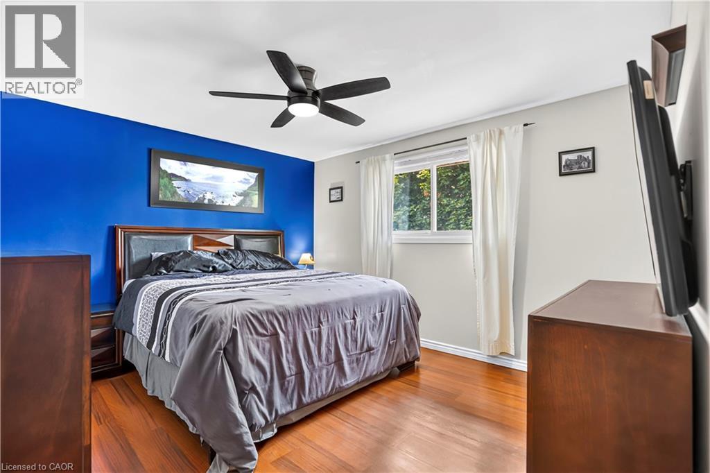 Wood-finish flooring throughout, featuring a bright window with white trim, a ceiling fan with integrated lighting, and a prominent accent wall - 234 Thunderbird Drive, Cambridge, ON - Indoor Photo Showing Bedroom
