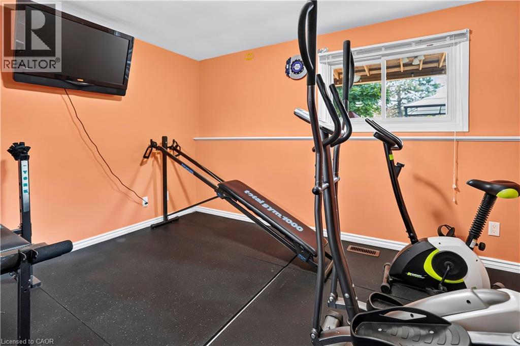 Dedicated interior space featuring resilient black flooring, a wall-mounted television, and a window with white trim - 234 Thunderbird Drive, Cambridge, ON - Indoor Photo Showing Gym Room