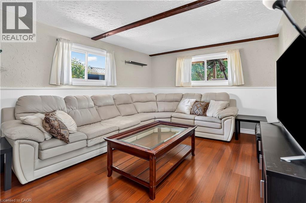 Living area featuring rich wood-finish flooring, white base molding, two windows, and exposed ceiling beams - 234 Thunderbird Drive, Cambridge, ON - Indoor Photo Showing Living Room
