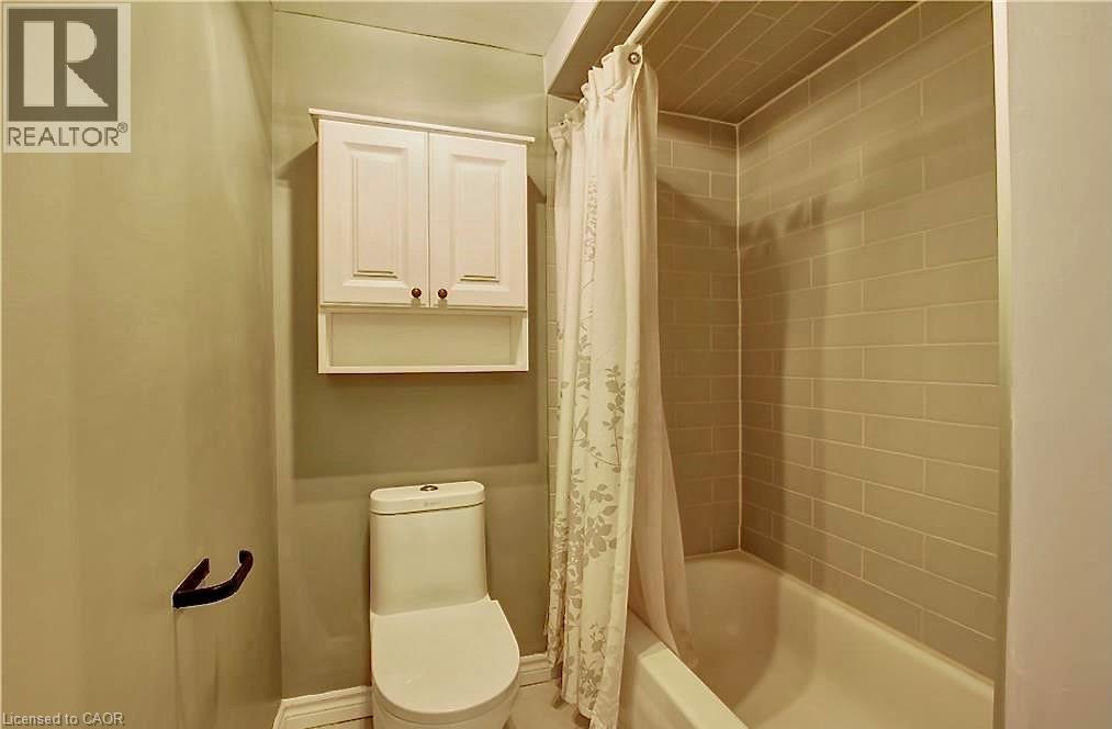 Bathroom featuring a white bathtub, subway tile surround, white toilet, and a wall-mounted white cabinet with decorative hardware - 599 Upper Horning Road Unit# Main/Upper, Hamilton, ON