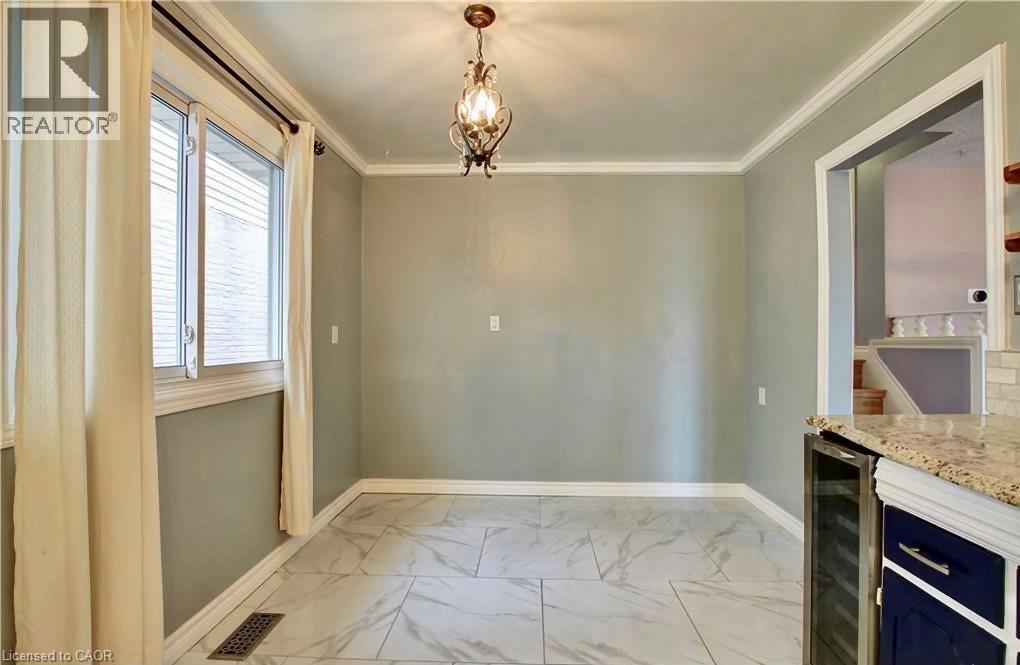 Dining area featuring large format white tile flooring, crown molding, a decorative chandelier, and a built-in beverage cooler with a granite countertop - 599 Upper Horning Road Unit# Main/Upper, Hamilton, ON