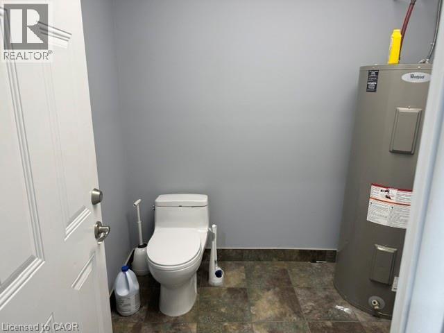 Restroom featuring a white toilet with a closed-lid design, light gray walls, and dark-toned tile flooring - 95 Hempstead Drive Unit# 9, Hamilton, ON