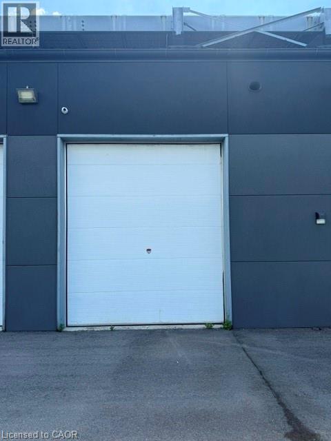 White sectional overhead door set into a dark gray facade with an asphalt parking surface - 95 Hempstead Drive Unit# 9, Hamilton, ON