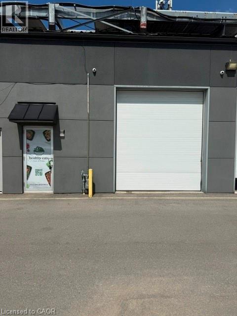 Commercial building featuring a roll-up garage door, pedestrian entrance with awning, exterior lighting, and security camera - 95 Hempstead Drive Unit# 9, Hamilton, ON