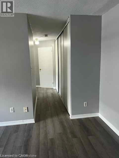 Hallway featuring dark wood-finish flooring, light grey painted walls, white baseboards, and a series of sliding closet doors - 529 Parkside Drive Unit# 7, Waterloo, ON