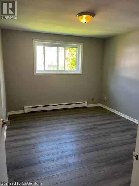 Spacious room featuring wood-finish flooring, a white-framed window, and a wall-mounted baseboard heater - 529 Parkside Drive Unit# 7, Waterloo, ON