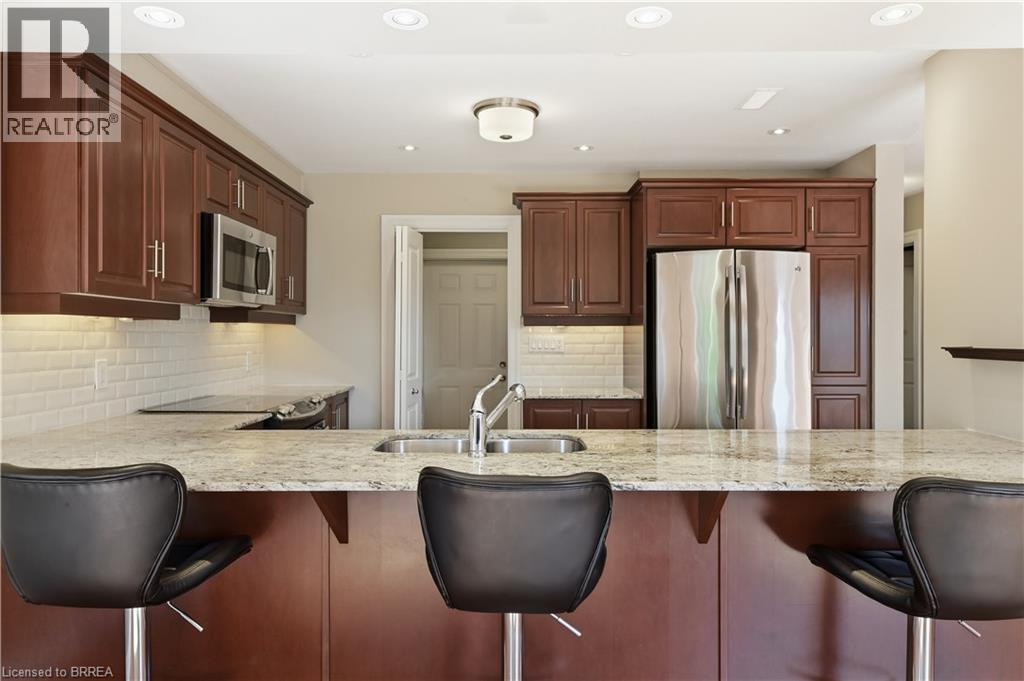 Kitchen featuring a granite-look island, stainless steel sink with a high-arc faucet, rich wood cabinetry, stainless steel appliances, and subway tile backsplash - 29 Archdeacon Clark Trail, Hamilton, ON