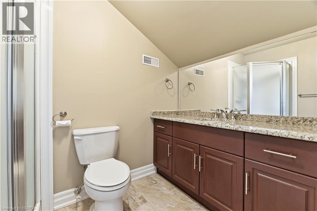 Bathroom with an elongated toilet, a glass-enclosed shower, a double vanity with stone countertop, dark wood-finish cabinetry, and a large mirror - 29 Archdeacon Clark Trail, Hamilton, ON