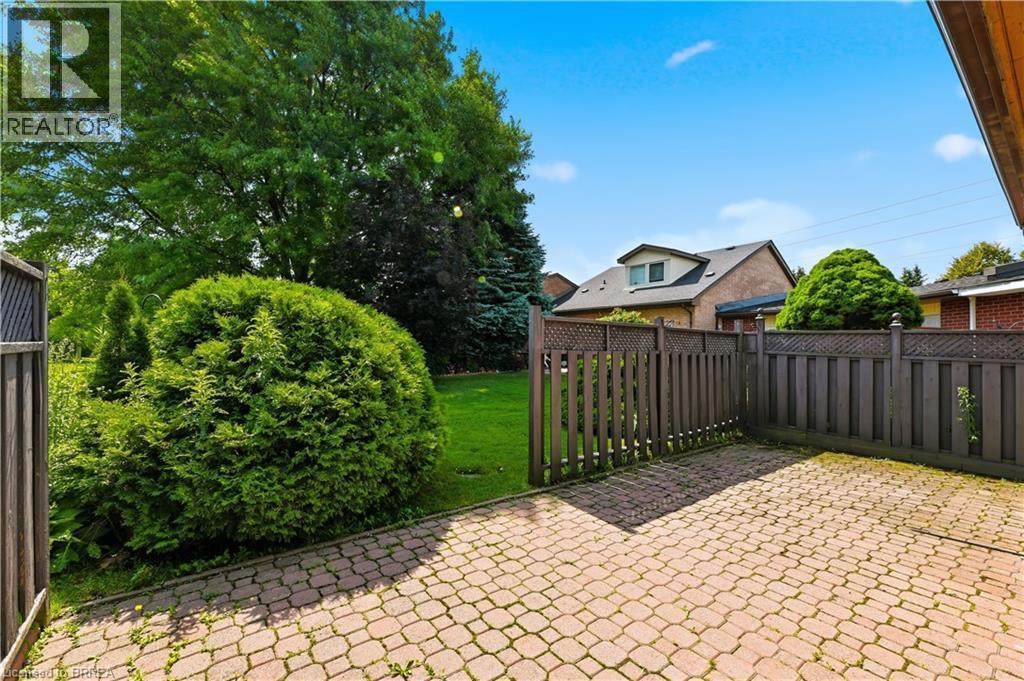 Brick paver patio and walkway bordered by a wooden privacy fence and established shrubbery - 29 Archdeacon Clark Trail, Hamilton, ON