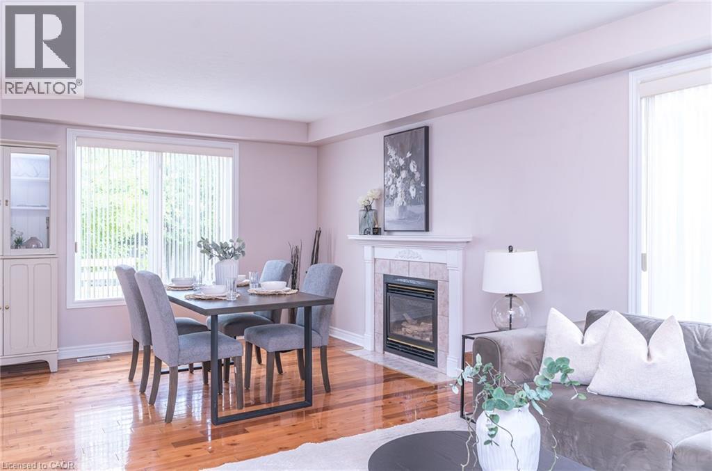 Open-concept living space featuring wood-finish flooring, a built-in fireplace with a stone surround and mantel, and a large window with vertical blinds - 566 Avignon Place, Waterloo, ON