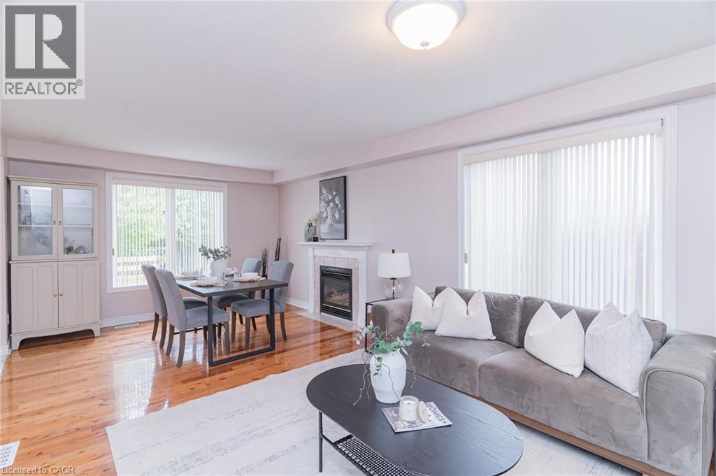 Open-concept living space featuring wood-finish flooring, a white fireplace with a tiled surround, a large window with vertical blinds, and a built-in display cabinet with glass doors - 566 Avignon Place, Waterloo, ON