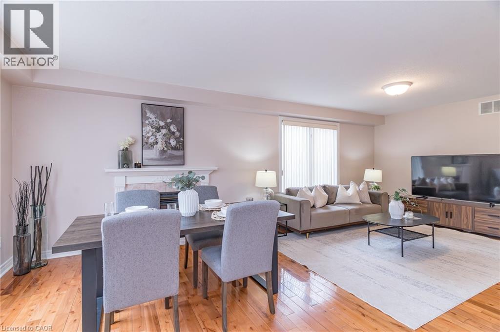 Open concept living and dining area featuring wood-finish flooring, a built-in fireplace mantel, and large windows with privacy blinds - 566 Avignon Place, Waterloo, ON