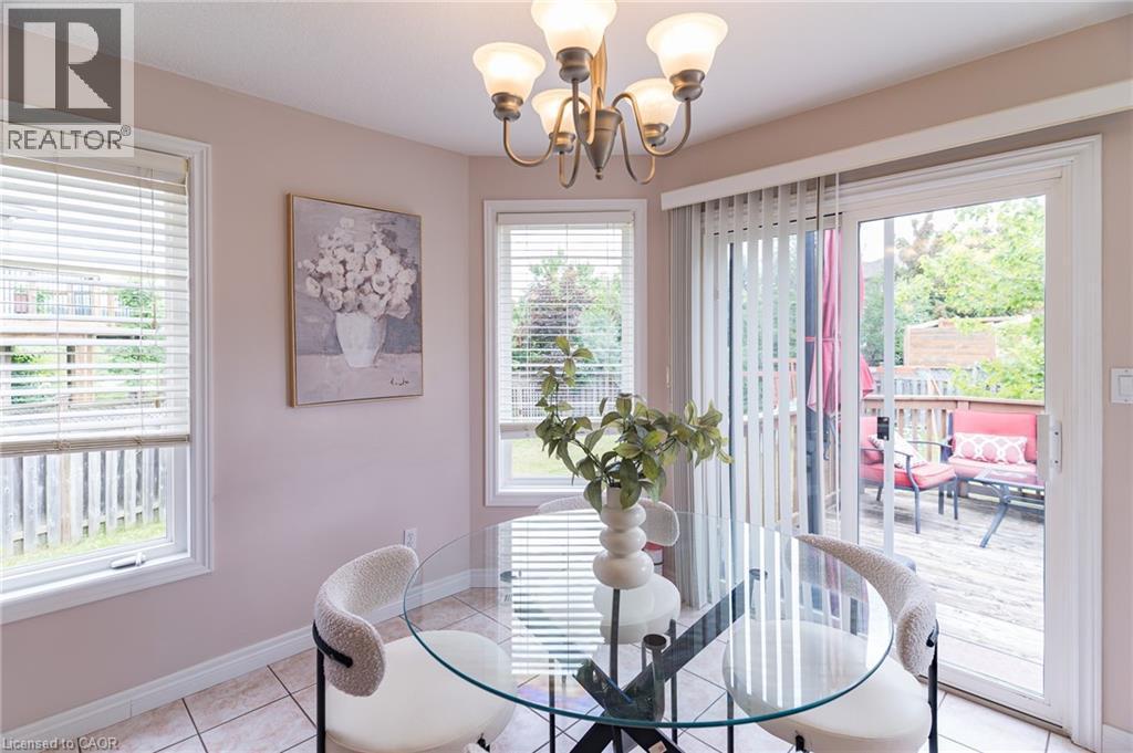 Dining area featuring tile flooring, a multi-light chandelier, two windows with blinds, and a sliding glass door providing access to an outdoor deck - 566 Avignon Place, Waterloo, ON