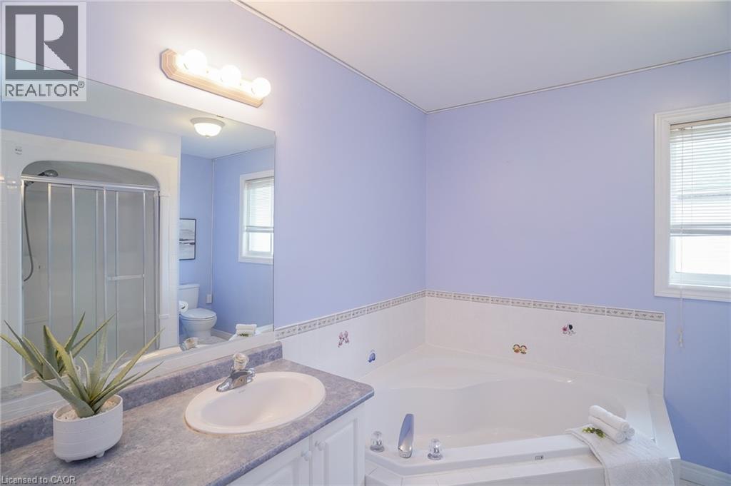 Bathroom featuring a corner soaking tub, a vanity with an integrated sink, a large wall-mounted mirror, a shower enclosure with sliding glass doors, and a window with horizontal blinds - 566 Avignon Place, Waterloo, ON