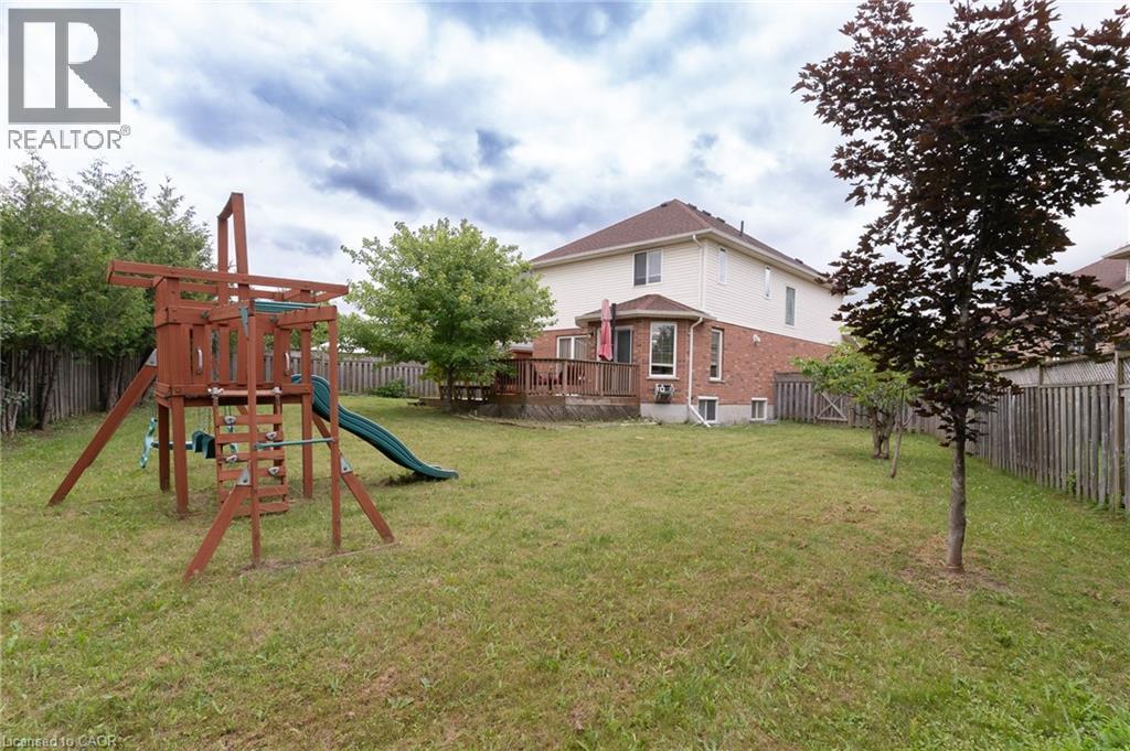 Expansive lawn area featuring a wooden playset with a slide, mature trees, and a wooden fence - 566 Avignon Place, Waterloo, ON
