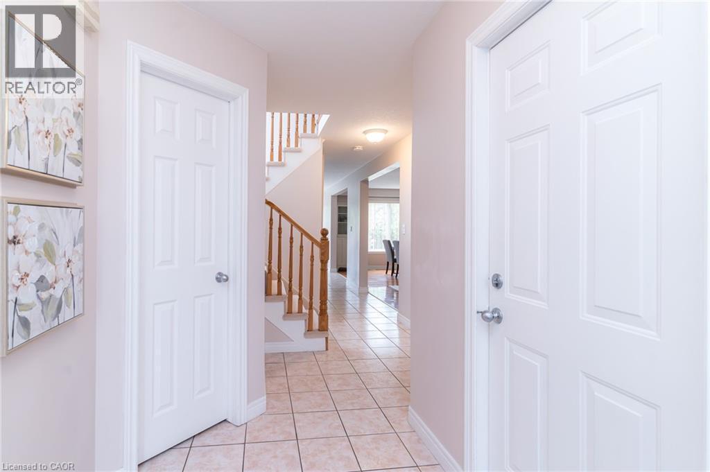 Foyer featuring light-toned square tile flooring, white six-panel doors, and a wood staircase with balusters - 566 Avignon Place, Waterloo, ON