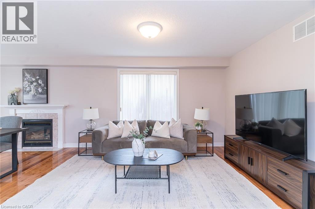 Living area featuring wood-finish flooring, a fireplace with a stone surround and mantel, and a sliding glass door - 566 Avignon Place, Waterloo, ON