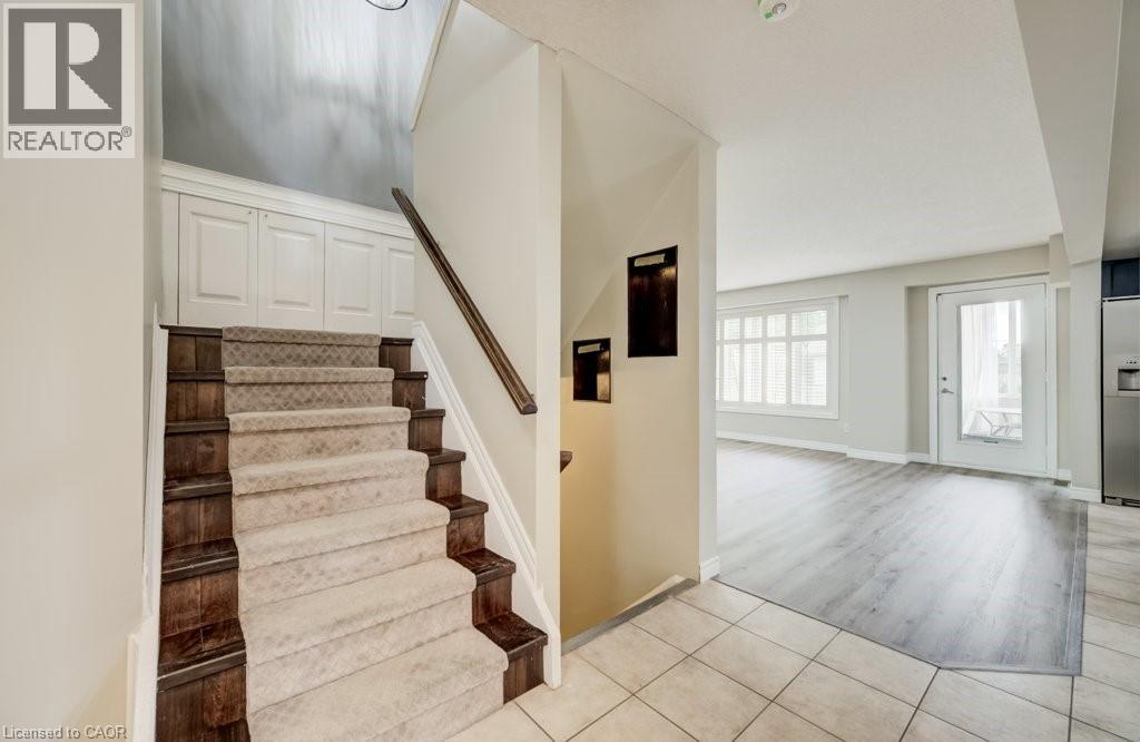 Entryway featuring a carpeted staircase with wood-finish risers and handrail, neutral tile flooring, and integrated wall paneling - 123 Forest Edge Trail, Kitchener, ON