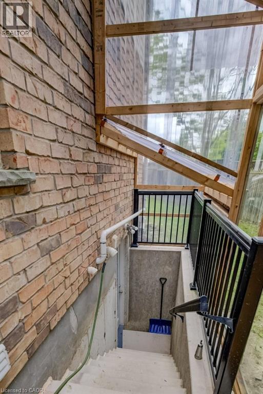Brick exterior with a clear panel enclosure and a concrete stairwell featuring black metal railings - 123 Forest Edge Trail, Kitchener, ON