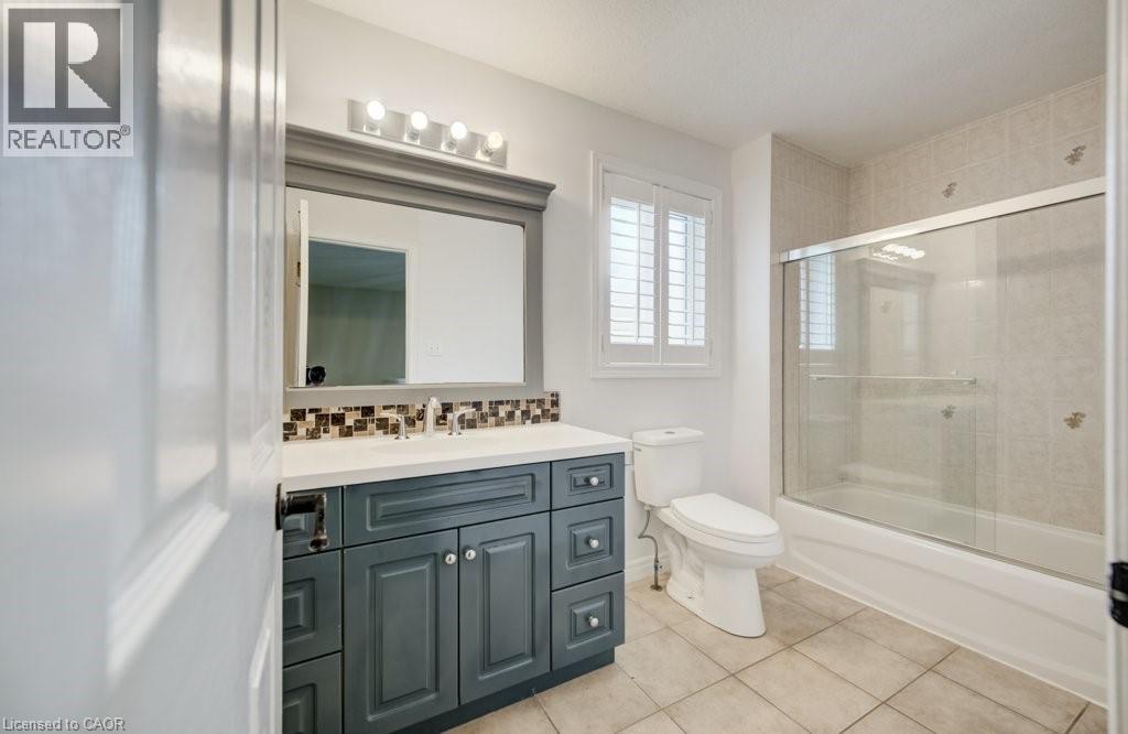 Bathroom featuring a vanity with a white countertop, mosaic tile backsplash, framed mirror, and a four-bulb light fixture - 123 Forest Edge Trail, Kitchener, ON
