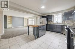 Open-concept kitchen and living area featuring high-gloss gray cabinetry, stainless steel appliances, a center island with wood-finish countertop, and tile flooring -