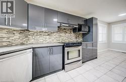 Kitchen featuring gray cabinetry with brushed nickel hardware, a mosaic tile backsplash, and light-toned tile flooring -
