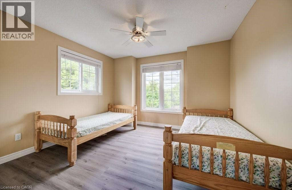 Room featuring wood-finish flooring, two large windows with white trim, and a ceiling fan with integrated lighting - 123 Forest Edge Trail, Kitchener, ON - Indoor Photo Showing Bedroom